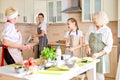 Positive teen girl washes the dishes while others prepare food at table