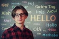 Positive teen guy wearing red shirt and eyeglasses over grey wall background and the word hello written in different languages and