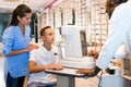 Teenage boy with worried mother receiving eye examination on modern refractometer in optical store with professional Royalty Free Stock Photo