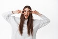 Positive teenage girl with long hair, shows peace v-signs and smiles happy at camera, dances joyful, white background Royalty Free Stock Photo