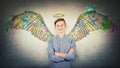 Positive teenage student boy keeps hands folded, tooth smile imagine himself an angel with fluffy wings behind back and a halo Royalty Free Stock Photo