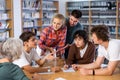 Positive teenage students working and discussing in groups in library Royalty Free Stock Photo