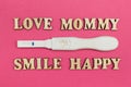 A positive test for pregnancy and the words `love, mommy, smile, happy` made of wooden letters on a pink background