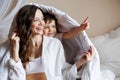 Positive toddler boy pointing away near mother holding blanket on bed at home Royalty Free Stock Photo