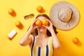 Positive unknown woman wearing striped swimming suit lying with oranges sunscreen on yellow background covering eyes with fruit Royalty Free Stock Photo