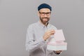 Positive unshaven man has stubble, carries boxes with present, opens one of them, has happy facial expression, wears formal white