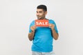 Positive unshaven man holding sale card in hands looking at camera with toothy smile, black friday.