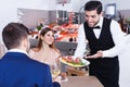 Positive waiter serving seafood meals to guests