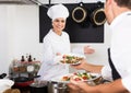 Positive woman cook giving salad to waitress Royalty Free Stock Photo