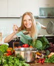 Positive woman cooking with ladle from raw vegetables