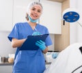 Positive woman cosmetician standing in office with clipboard