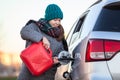 Positive woman driver pouring petrol from red plastic gasoline can into a car tank