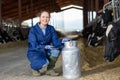 Positive woman farmer squatting at milk can