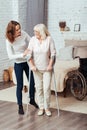 Positive woman helping he grandmother to walk with crutches