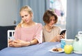 Positive woman and her teenage son looking absorbedly at phones at table Royalty Free Stock Photo