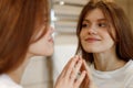 Positive woman in the morning looks at the reflection in the mirror, facial skin care