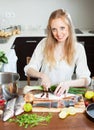 Positive woman slicing raw fish at kitchen table Royalty Free Stock Photo