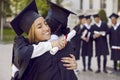 Positive women graduates in student gown hug each other after graduating from university or college Royalty Free Stock Photo