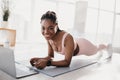 Positive young African American woman standing in elbow plank at home, using laptop for online training video Royalty Free Stock Photo