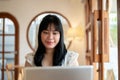A positive young Asian woman is working remotely at a coffee shop, using her laptop computer Royalty Free Stock Photo