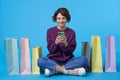 Positive young attractive curly brunette woman holding mobile phone in raised hands and looking cheerfully on screen, sitting over