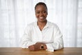 Positive young black woman sitting at workdesk at office