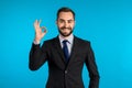 Positive young businessman smiles to camera. Man showing OK sign over blue background. Winner. Success. Body language. Royalty Free Stock Photo