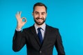 Positive young businessman smiles to camera. Man showing OK sign over blue Royalty Free Stock Photo