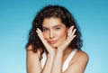 Positive young caucasian curly woman touching face with hands, enjoy result of beauty care