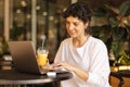 Positive young caucasian girl uses her laptop sitting in cafe. Royalty Free Stock Photo