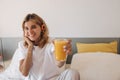 Positive young caucasian woman listening music holds glass of orange juice in hand indoor. Royalty Free Stock Photo