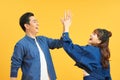 Positive young couple give high five, agree to work as team, stand sideways, on yellow wall. Male student with notepad