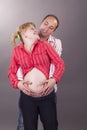 Happy Positive Young Couple Standing Together Close While Hugging HEr Pregnant Woman And Wearing Casual Clothing Over Gray Royalty Free Stock Photo