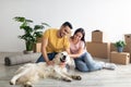 Positive young diverse couple stroking their dog in new home on moving day, full length. Home relocation concept Royalty Free Stock Photo