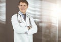 Positive young doctor is smiling at camera. Portrait of professional physician in sunny clinic