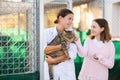 Female volunteer showing gray tabby cat to girl in outdoor shelter