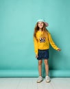 Pretty fashionable young teenager with a lovely smile posing in a baseball cap and yellow hoodie on a blue background Royalty Free Stock Photo