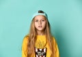 Pretty fashionable young teenager with a lovely smile posing in a baseball cap and yellow hoodie on a blue background Royalty Free Stock Photo