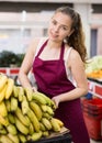 Positive young girl a salesperson puts bananas on the counter