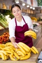 Young female owner of store laying out bananas on display