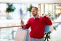 Positive young guy with gift bags using cellphone at mall, taking selfie or photo, having video call, free space Royalty Free Stock Photo