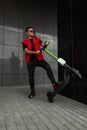 Positive young hipster man with hairstyle in stylish denim red-black clothes in sunglasses poses with a modern electric scooter Royalty Free Stock Photo