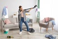 Positive young lady holding vacuum cleaner like rifle, ready to perform cleanup at messy room after party, copy space
