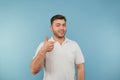Positive young man with bristles in a white T-shirt stands on a blue background and shows a gesture like with a smile on his face Royalty Free Stock Photo