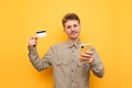 Positive young man with glasses and mustache holding credit card and smartphone, looking into camera and smiling against yellow Royalty Free Stock Photo