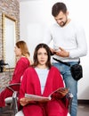 Positive young man hairdresser cuts hair of young woman with magazine at salon Royalty Free Stock Photo