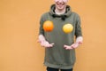 Positive young man juggles with lemon and orange on the background of an orange wall. Concept Fruit