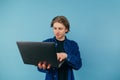 Positive young man with a laptop in his hands stands on a blue background and works, looking at the screen with a smile Royalty Free Stock Photo