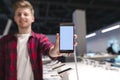 positive young man sends a smartphone with a white screen to the camera and smiles
