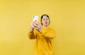 Positive young man taking selfie on smartphone camera on yellow background and making funny face, wearing yellow sweatshirt Royalty Free Stock Photo